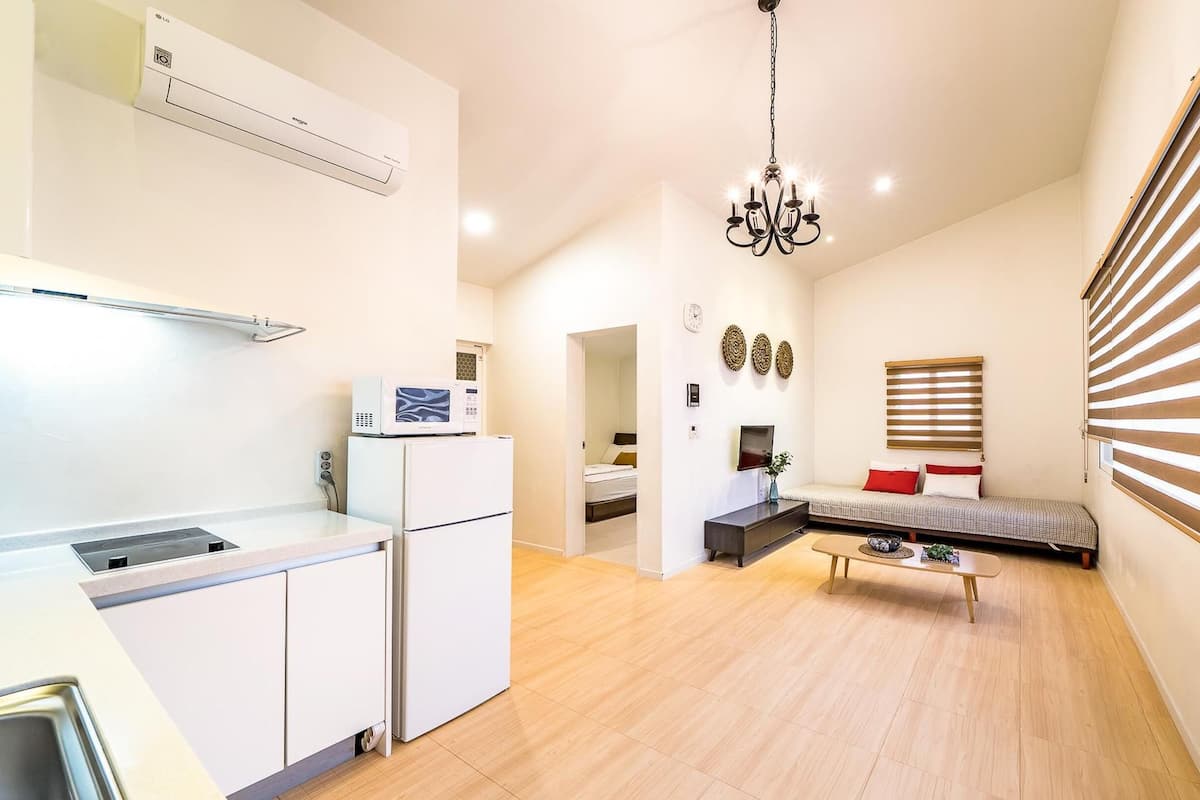 A compact living space with a kitchenette, a dining area, a seating area with a sofa and a TV, and a window with blinds.