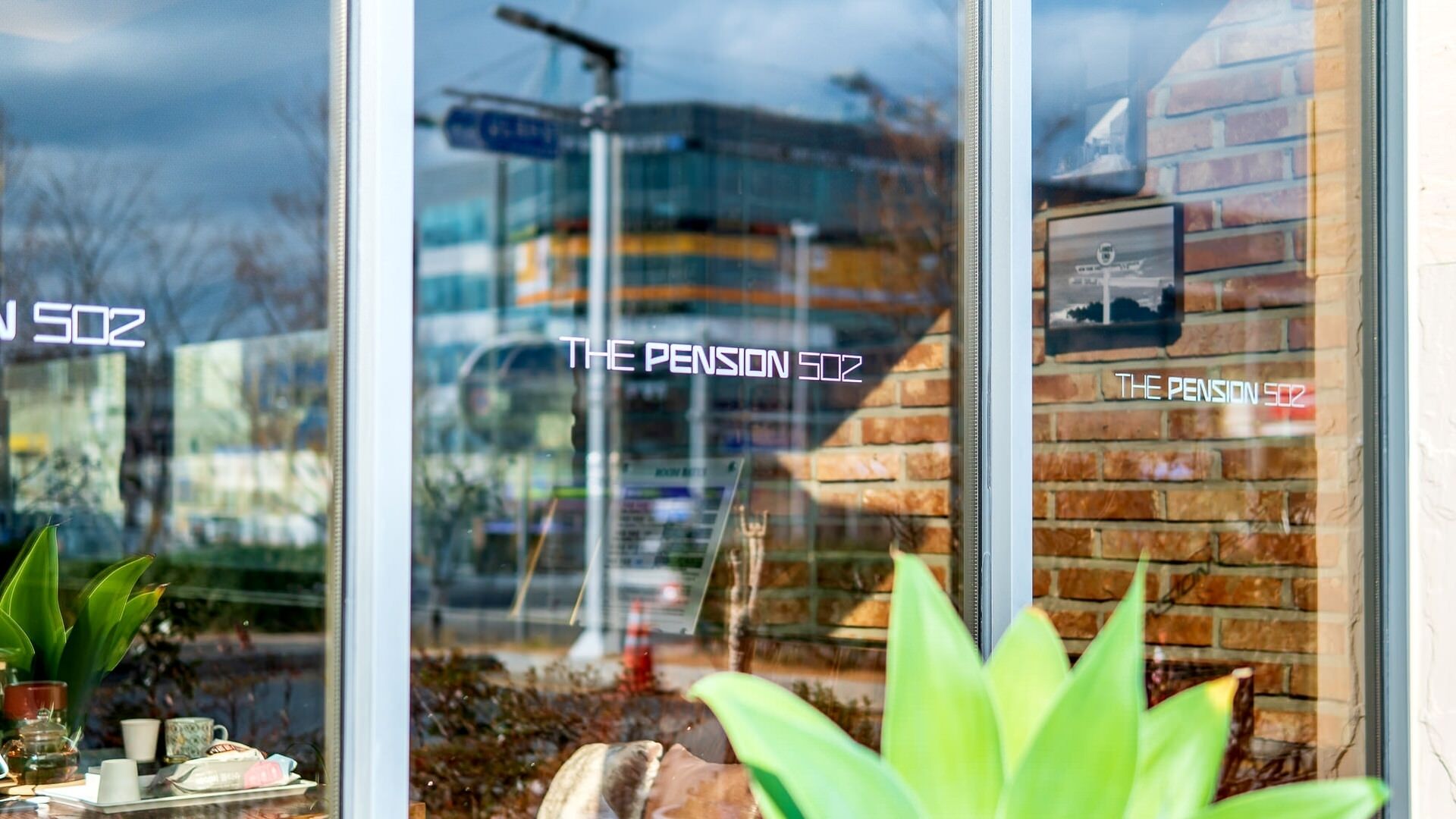 Una ventana con reflejos de una señal de calle y un edificio, y el texto 'THE PENSION 502' en el cristal.