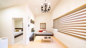 Une chambre d’hôtel moderne équipée d’un lit, d’un petit coin salon, d’une table à manger et d’une grande fenêtre avec des stores.