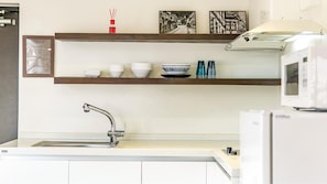 A modern kitchen with a stainless steel sink, white cabinets, and a microwave. There are two shelves above the sink holding dishes and a small decorative item. - Busan the Pension 502 (Busan)