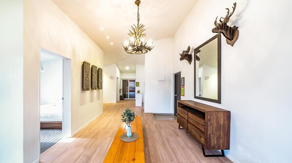 A hallway with a wooden floor, a chandelier, a mirror, and a wooden console table. - Busan the Pension 502 (Busan)