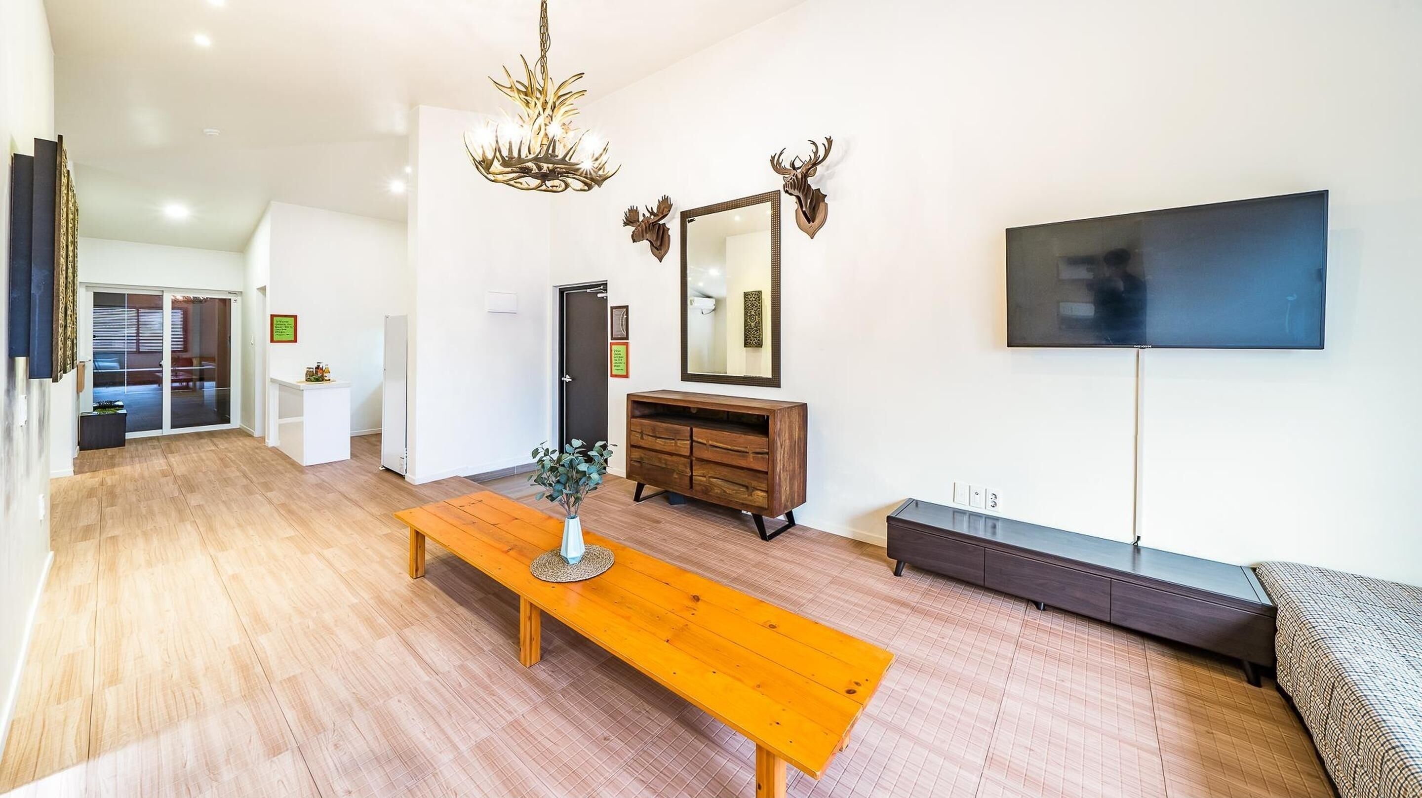 A spacious living room with a wooden bench, a TV mounted on the wall, and a large mirror with antler decorations.