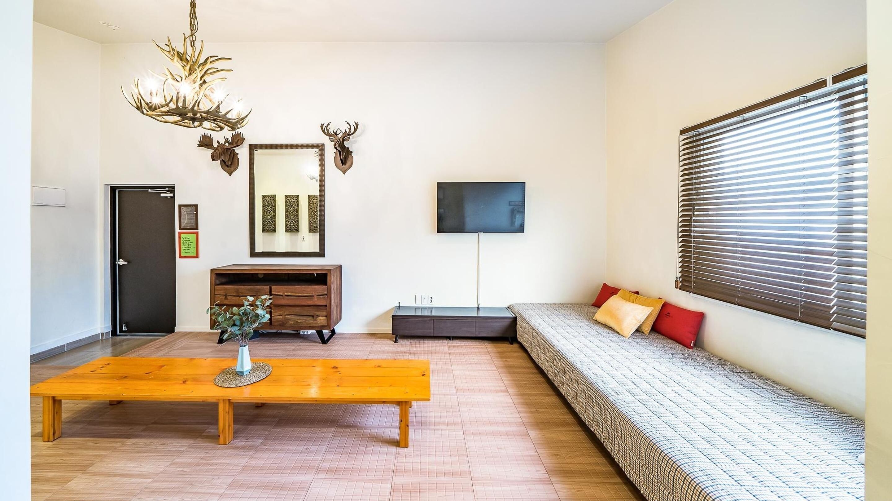 A modern living room with a wooden coffee table, a sofa with patterned cushions, a mounted TV, and a decorative chandelier.