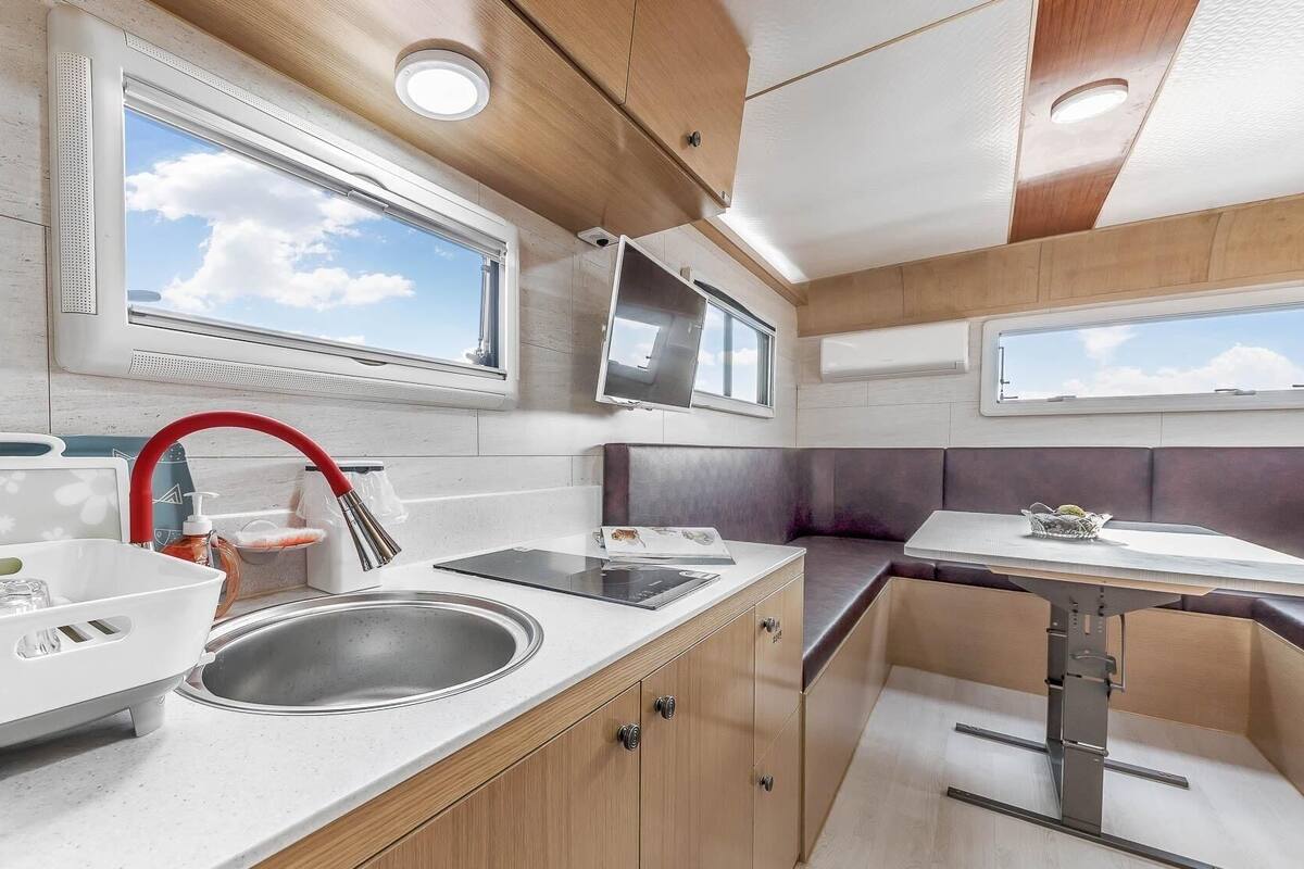 A compact kitchen with a sink, a red faucet, a window, and a flat-screen TV.