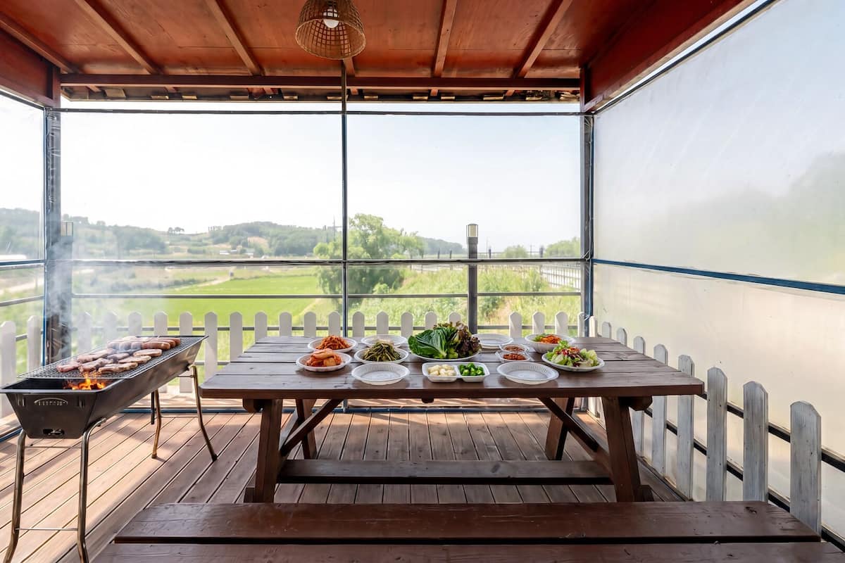 A covered outdoor dining area with a grill, wooden table, and various dishes.