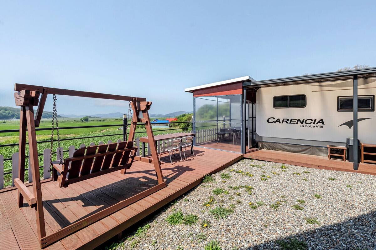 A covered outdoor area with a swing set, a table with chairs, and a view of a caravan labeled 'CARENCIA La Dolce Vita.'