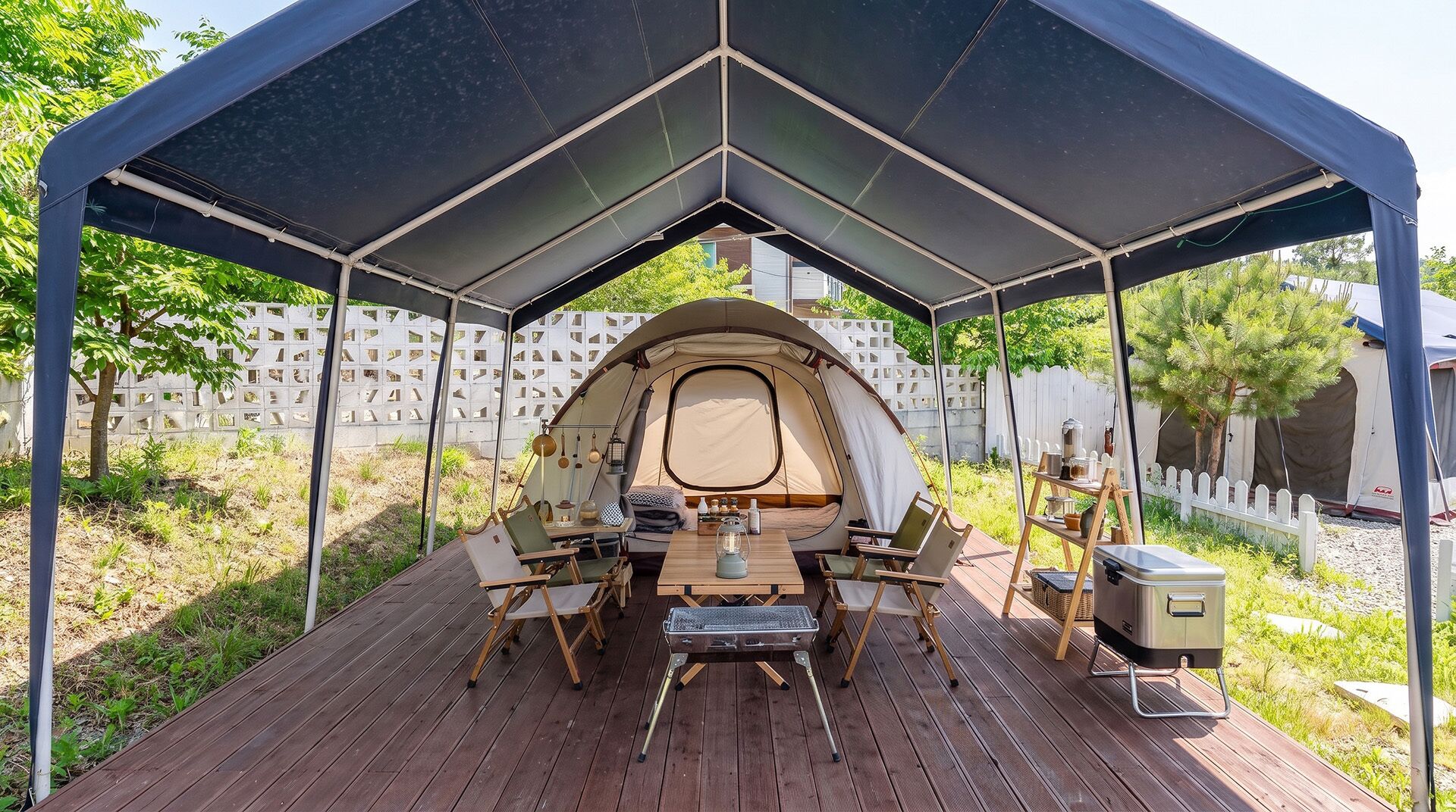 Un'area campeggio riparata con una tenda, un pontile in legno e mobili da esterno.