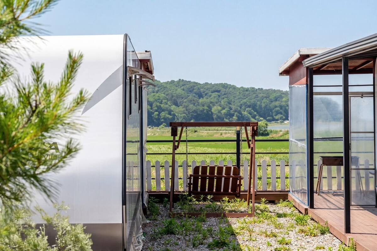 A balcony with a view of a lake and forest, a pergola, and a greenhouse structure.