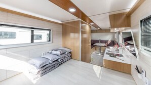 A compact RV interior with a bed, a kitchenette, a window, and a bathroom. - Ganghwa Nakjohealing Caravan&camping (Incheon)