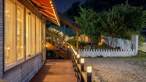 A building with a wooden deck, a white picket fence, and a covered area with string lights. - Ganghwa Nakjohealing Caravan&camping (Incheon)
