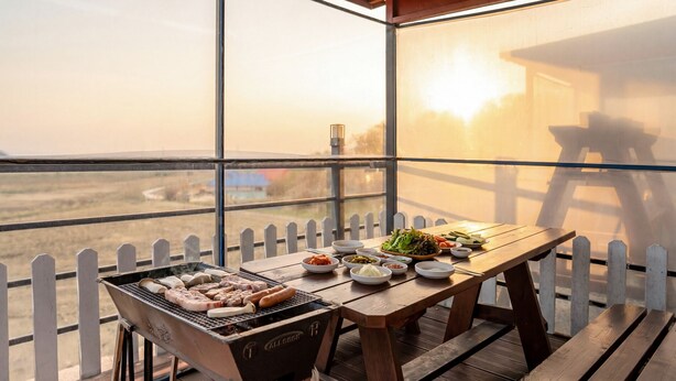 A balcony with a grill, dining table, and various dishes. - Ganghwa Nakjohealing Caravan&camping (Incheon)