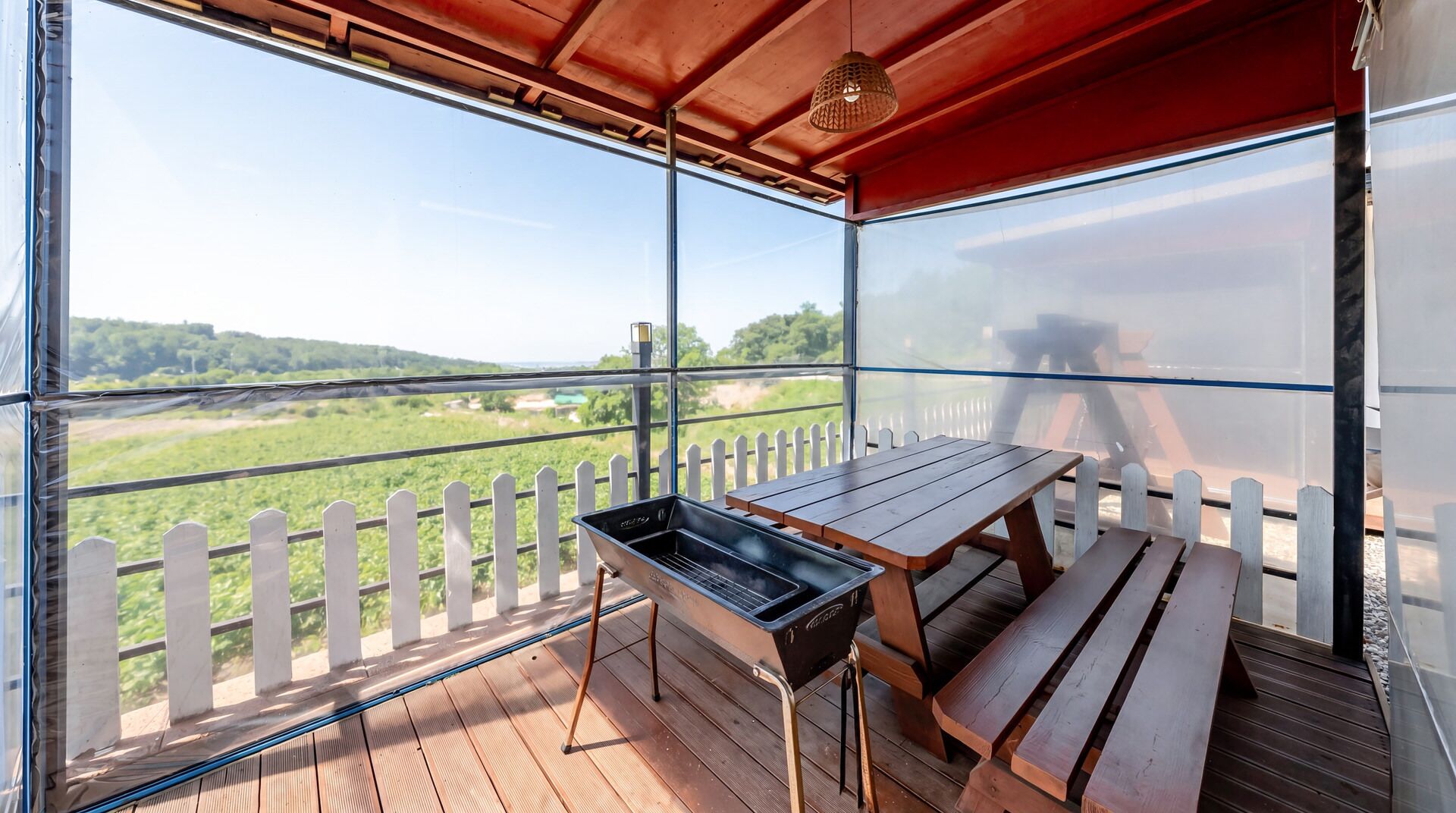 An outdoor patio with a grill, wooden benches, and a white picket fence.