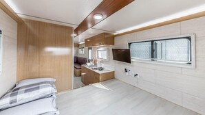 A compact RV interior with a kitchenette, a bed, and a window with a brick wall view. - Ganghwa Nakjohealing Caravan&camping (Incheon)
