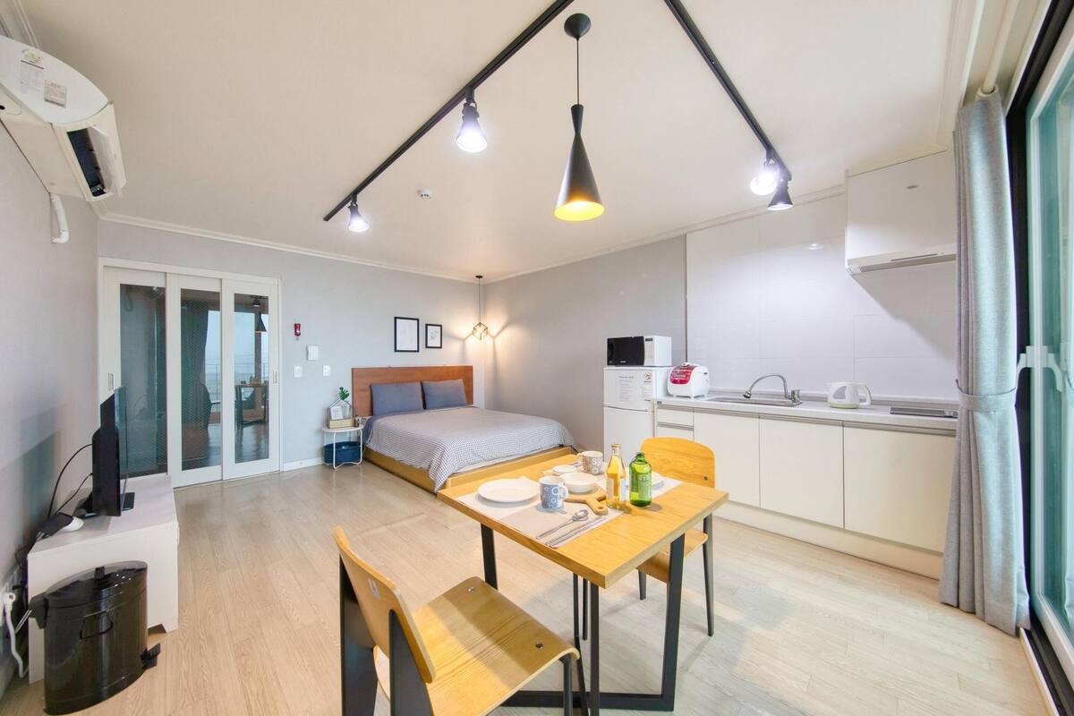 A compact room with a bed, a small kitchenette, a dining table, and a desk with a computer.
