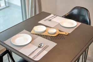 Una mesa de comedor dispuesta con platos, cubiertos y una tabla de madera para servir.