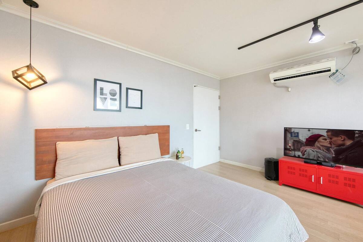 A bedroom with a bed, a red TV stand, and a ceiling light.