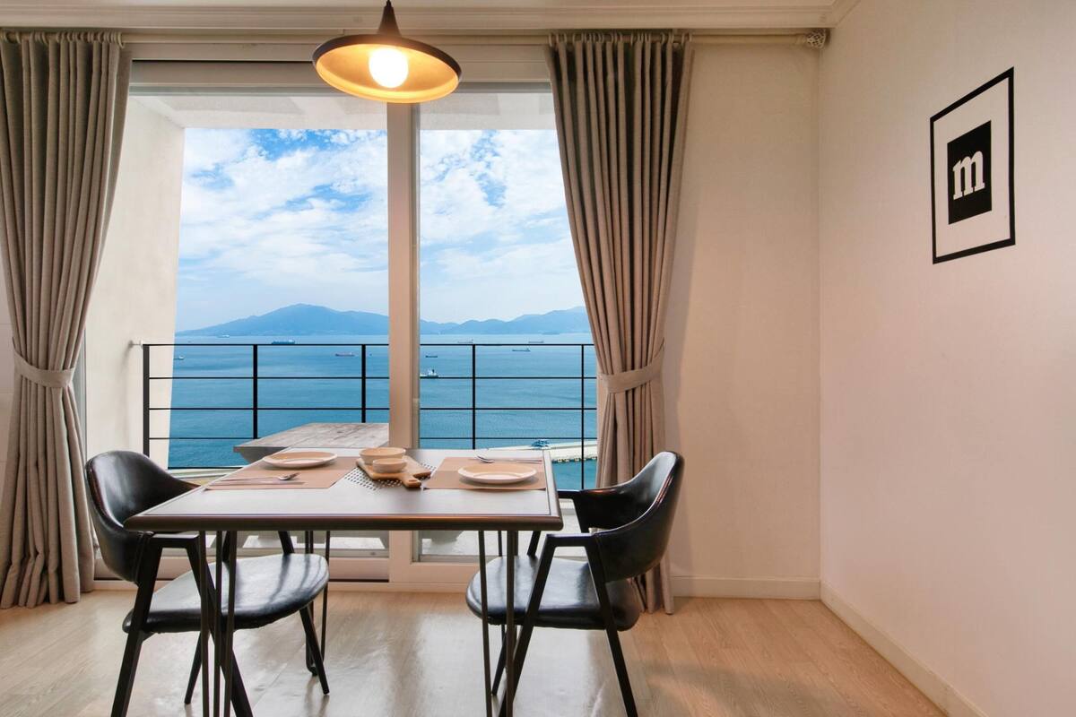 A dining area with a table, chairs, and a view of the sea through a large window.