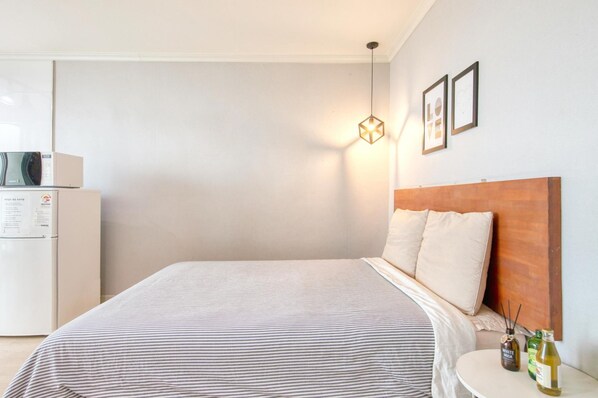 Une chambre d’hôtel équipée d’un lit, d’une table de chevet, d’une lampe fixée au mur et d’un réfrigérateur.