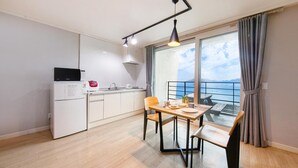 Cocina compacta con microondas, lavamanos y armarios. Hay una zona de comedor con mesa y sillas, y vistas al mar a través de ventanas amplias.