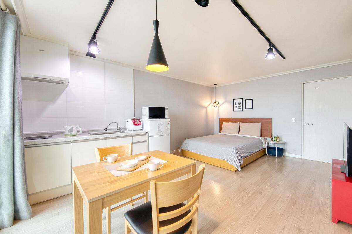 A compact hotel room with a kitchenette, a bed, a dining area, and a TV.