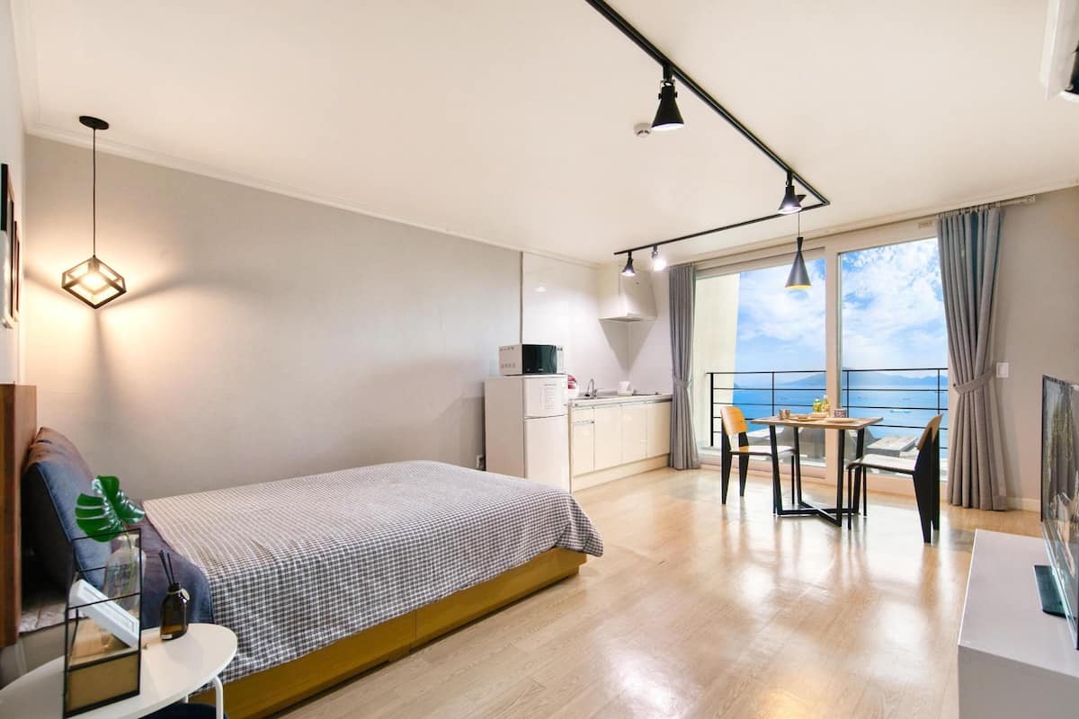 A modern bedroom with a bed, bedside table, and a view of the sea.