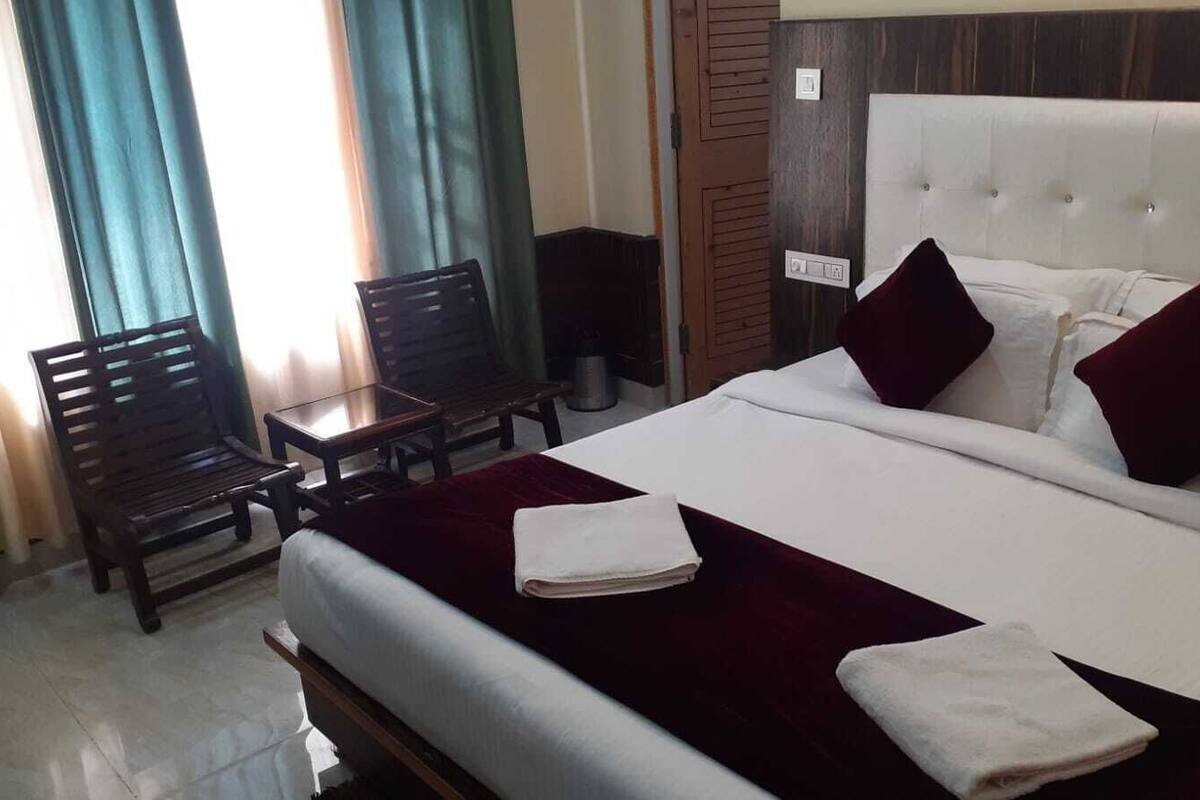 A hotel room with a bed, two pillows, a bedside table, a chair, and a window with curtains.