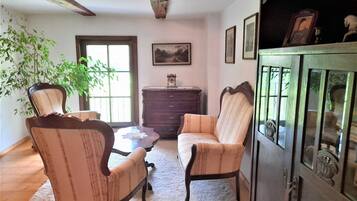 A room with two upholstered chairs, a wooden cabinet, a small table, and a window with a view.