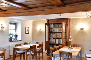 Una habitación con vigas de madera en el techo, una amplia estantería abierta y un comedor con mesas y sillas.