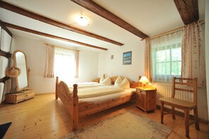 Un dormitorio con una cama de madera, una silla, una mesita de noche, una lámpara, un espejo y una ventana con cortinas.