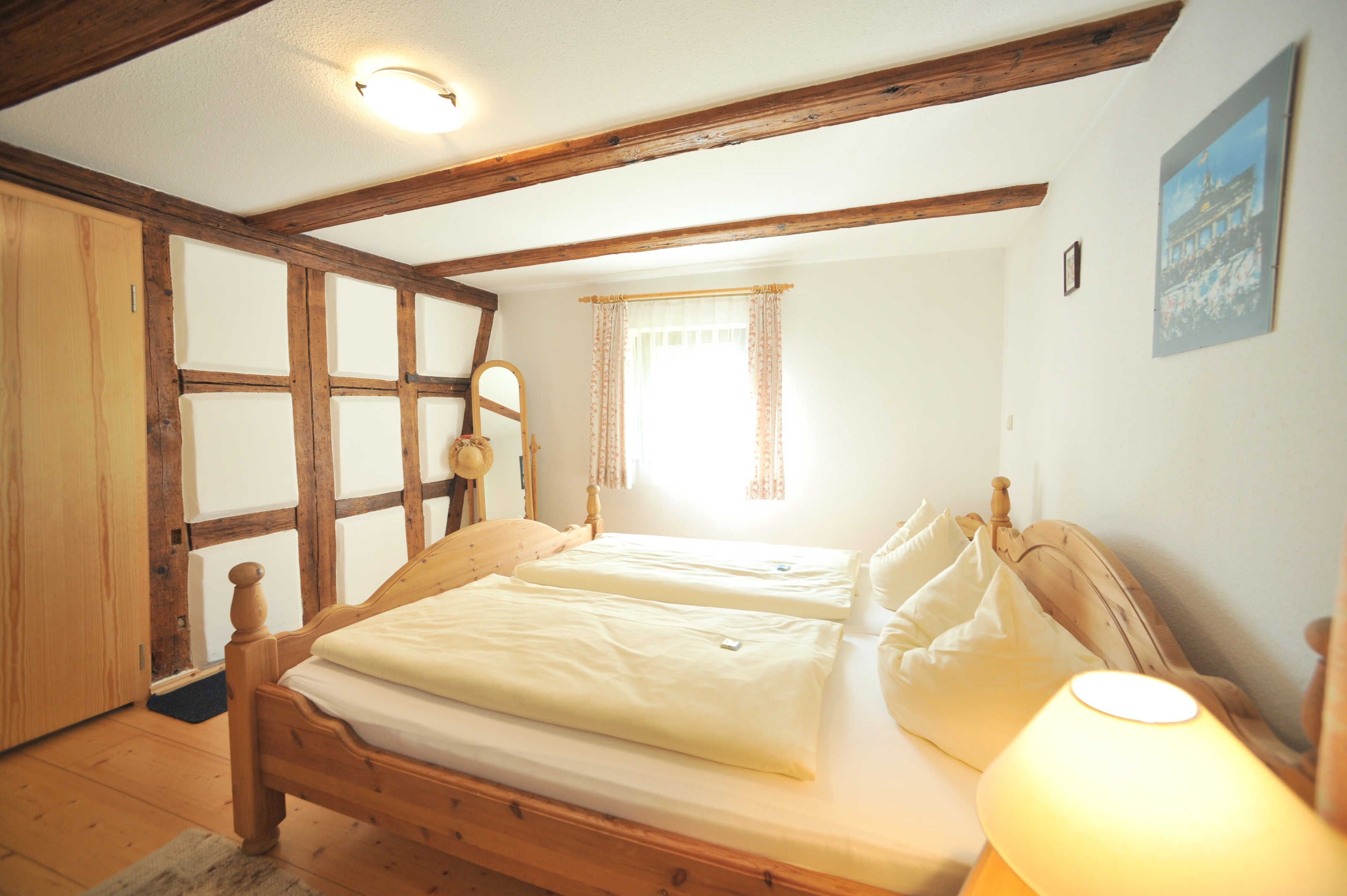 Une chambre à coucher avec un lit en bois, une table de chevet, une lampe et une fenêtre avec des rideaux.