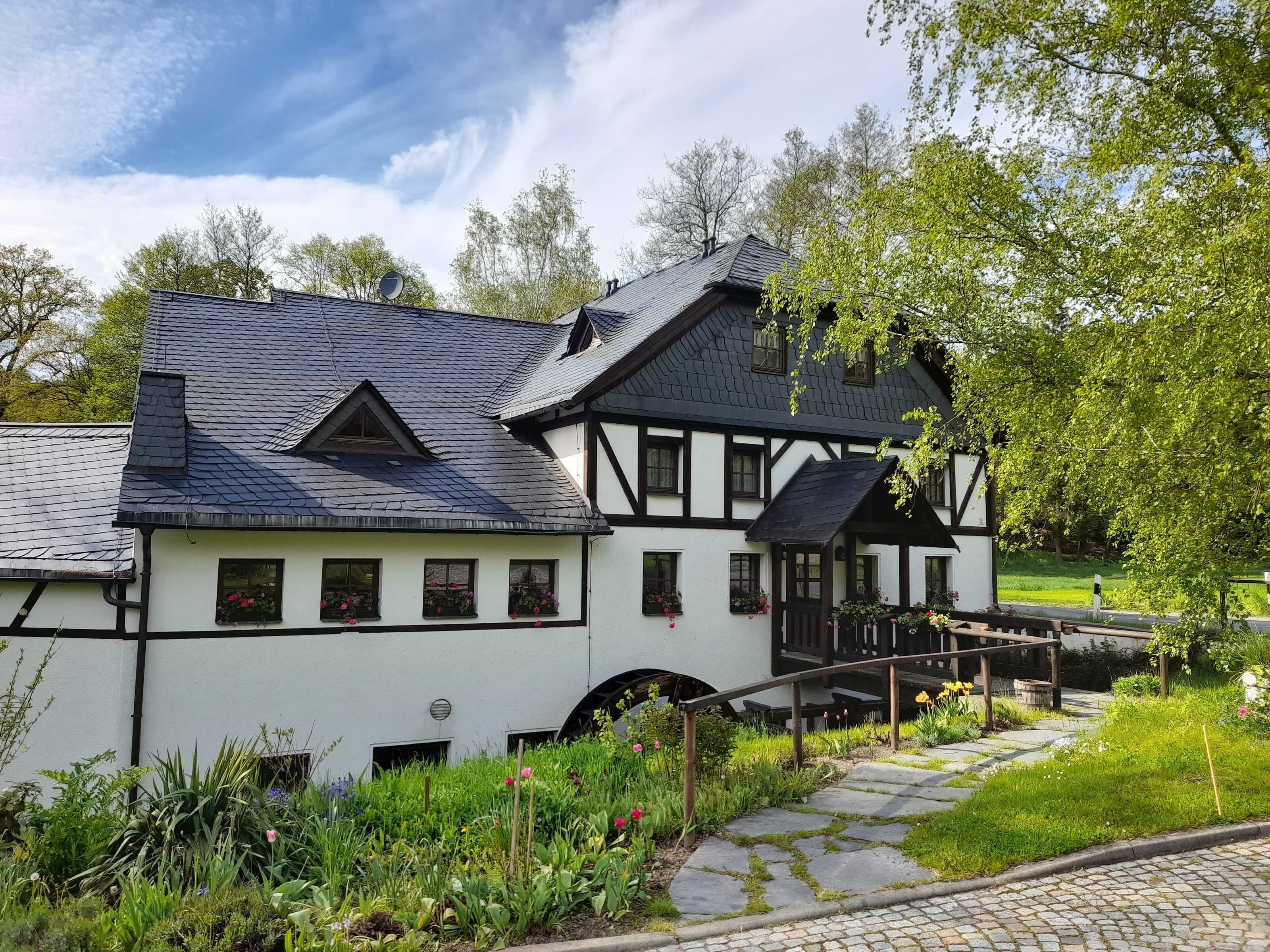 A traditional half-timbered house with a stone pathway leading to a wooden bridge.