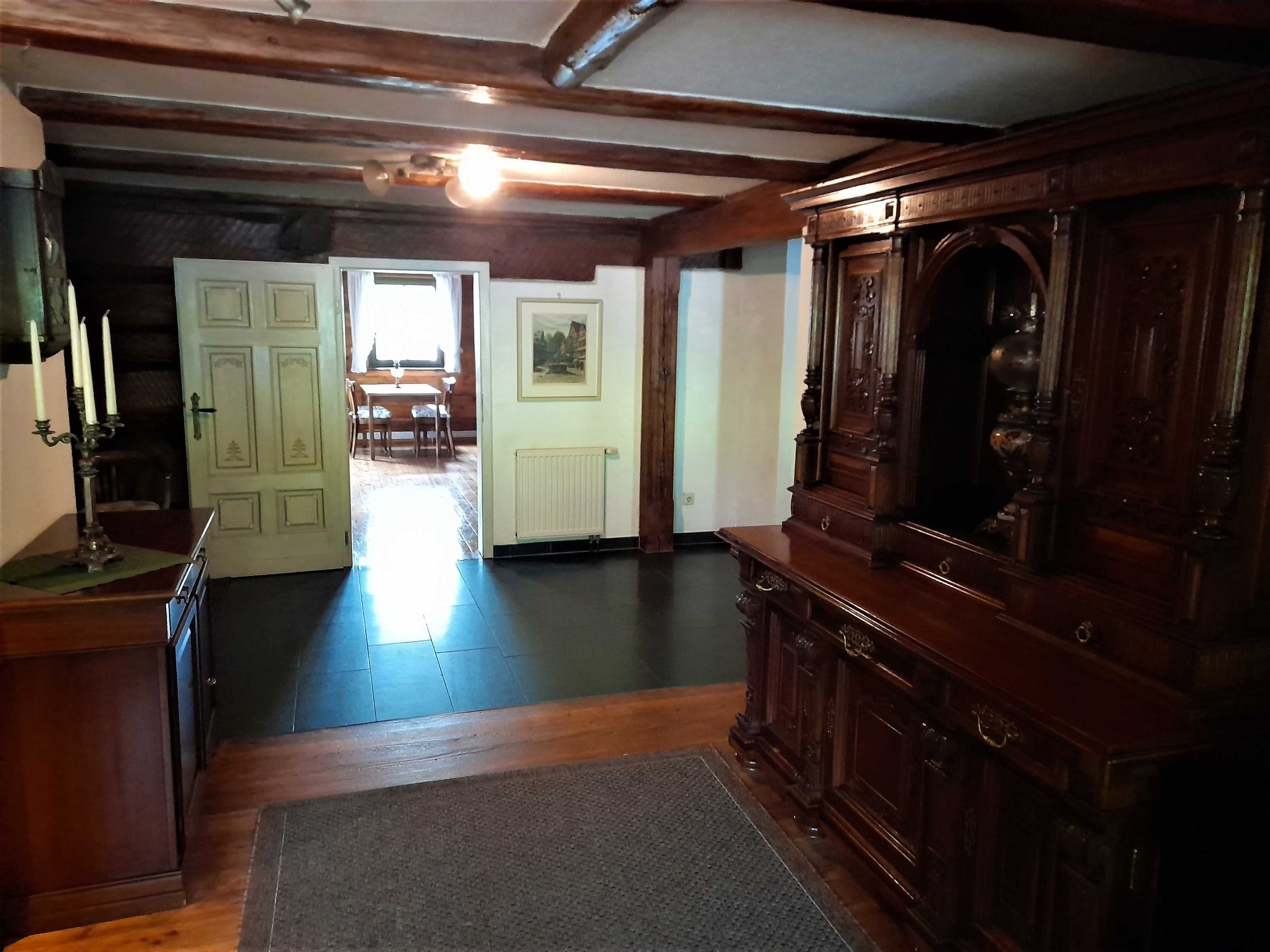 A room with wooden floors, a radiator, a wooden cabinet, and a door leading to another room.