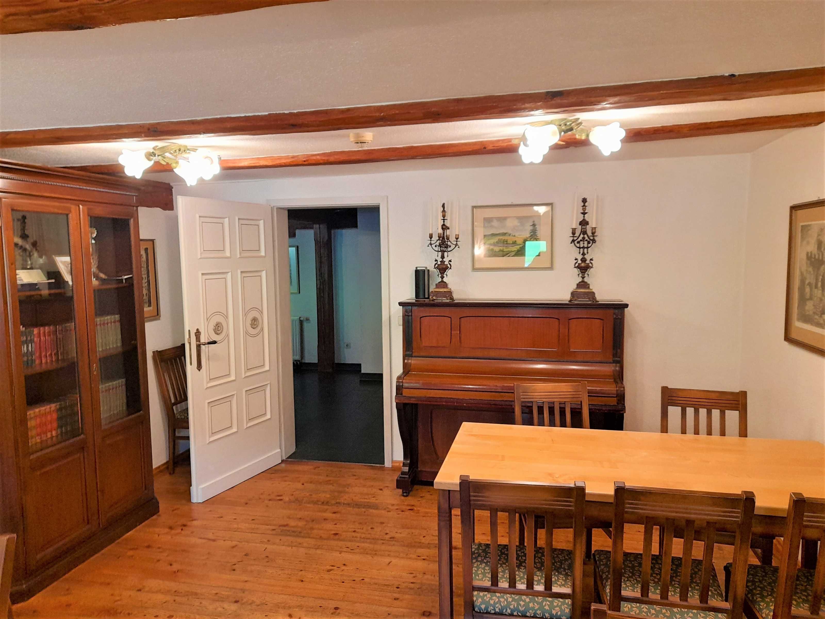 A dining area with a wooden table and chairs, a piano, and a cabinet with glass doors.