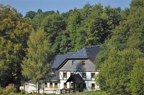 A traditional chalet with a steep roof, surrounded by dense forest.