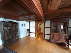 Una habitación amplia con suelo de madera, un mueble alto de madera con puertas de vidrio y una mesa pequeña con una planta.