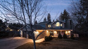 A two-story house with a garage, a front porch with string lights, and a well-maintained lawn. - Modern Midtown Home w/ Luxury Finishes & Hot Tub! (Bend)