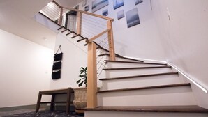 A staircase with wooden steps and a wooden handrail, leading to a landing with a black bag hanging on the wall. - Modern Midtown Home w/ Luxury Finishes & Hot Tub! (Bend)