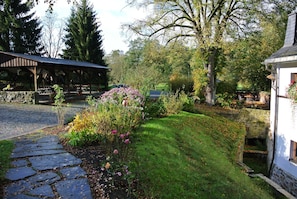 A stone pathway leading to a covered outdoor area with a rustic building, surrounded by lush greenery and flowering plants.