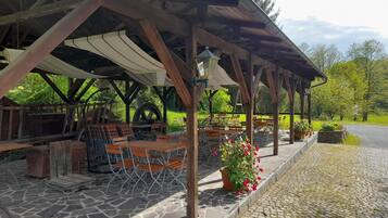 Un espace extérieur abrité, doté d’un sol en pierre et de tables et chaises en bois.