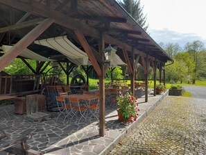 A covered outdoor seating area with stone flooring and wooden tables and chairs. - Doppelzimmer - Blaues Zimmer - Gasthof Teichmühle (Leubnitz)
