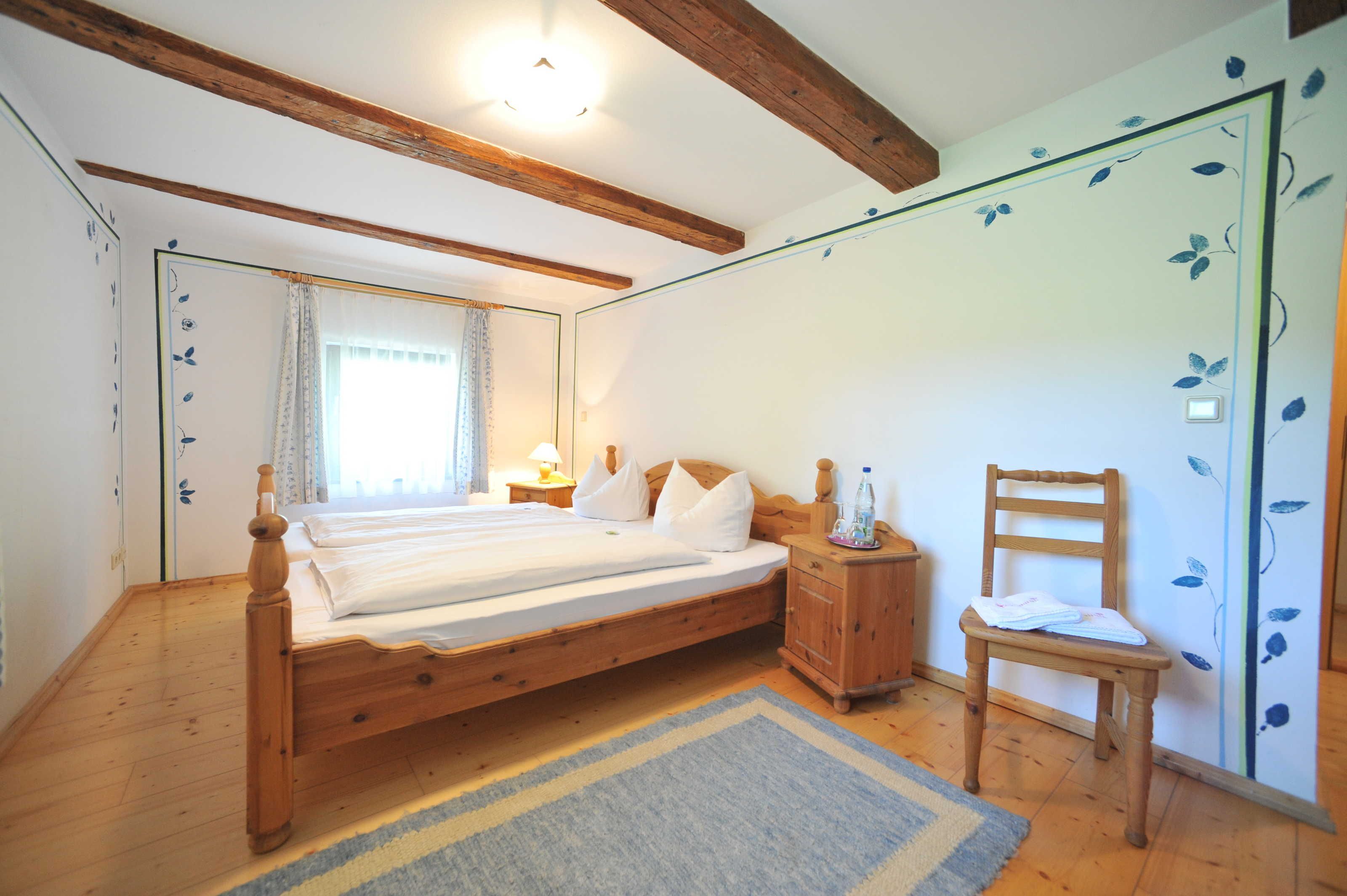 A bedroom with a wooden bed, a nightstand, a chair, and a wall with floral wallpaper.
