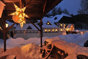 Un edificio cubierto de nieve con una lámpara en forma de estrella, vigas de madera y un banco cubierto de nieve.