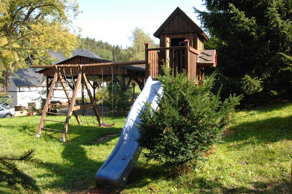 Un parque infantil con un tobogán, una estructura para escalar y un pequeño edificio de madera.