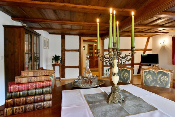 Un comedor con mesa de madera, libros, un candelabro y un televisor al fondo.