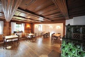 A wooden interior with multiple dining tables and chairs, a radiator, and a green decorative cabinet. - Doppelzimmer - Blaues Zimmer - Gasthof Teichmühle (Leubnitz)