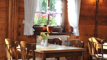 L’intérieur d’un chalet en bois, avec une table à manger, des chaises, une fenêtre avec des rideaux et une plante en pot.