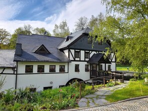 A traditional half-timbered house with a stone pathway leading to a wooden bridge. - Doppelzimmer - Grünes Zimmer - Gasthof Teichmühle (Leubnitz)