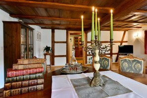 A dining area with a wooden table, books, a candelabra, and a television in the background.