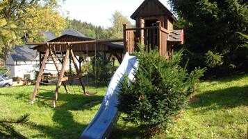 A playground with a slide, climbing structure, and a small wooden building.
