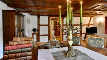 Un coin repas avec une table en bois, des livres, un chandelier et un téléviseur en arrière-plan.